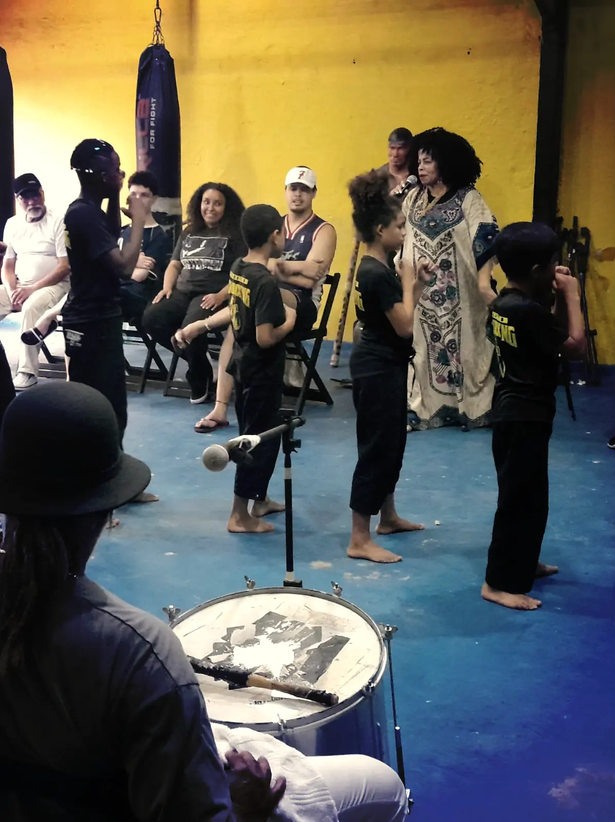 Professora e plateia ao fundo assistindo apresentação das crianças.